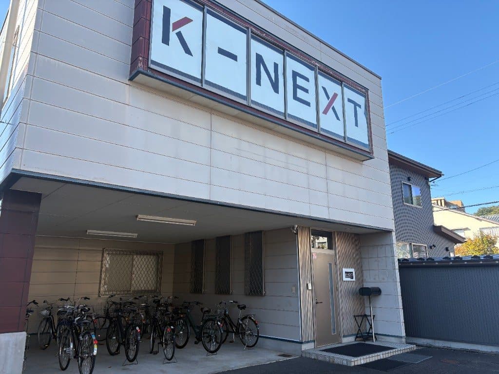 K-NEXTの校舎。外壁の看板と、自転車が並ぶ入口